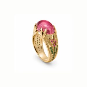 Gold ring with a large pink cabochon gemstone held by claw-like prongs and a textured, jewel-encrusted band.