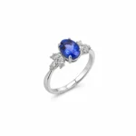 Silver ring featuring an oval blue sapphire centerpiece flanked by diamond clusters on a polished band.