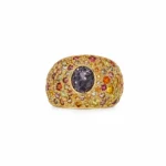 Gold ring covered with multicolored gems and a large round dark purple center stone.