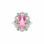 Ring with a large oval pink center stone surrounded by diamonds and teal accent stones on a silver band.