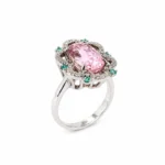 Ring with a large pink faceted center stone surrounded by a halo of small diamonds and green accents, set in silver metal.