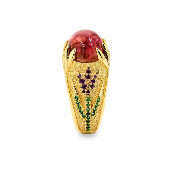 Gold ring featuring a large oval pink gemstone held by claw prongs, with intricate textured setting and rows of purple and green gemstones along the band